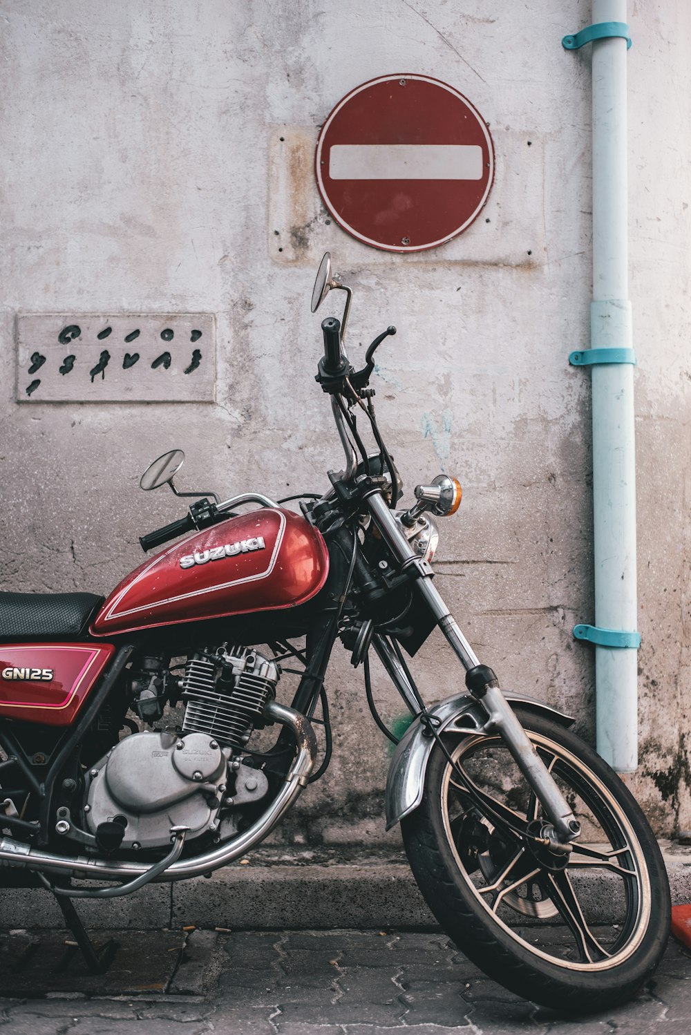 red and black Suzuki standard motorcycle parked besides white pipe