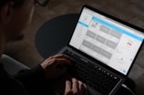 A person typing on a laptop with website designs on the screen.