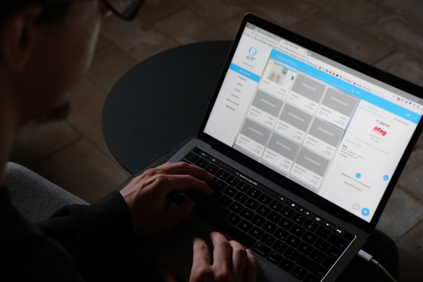 A person is using a laptop, typing with both hands on the keyboard. The screen displays a website layout with a grid of images and text panels.
