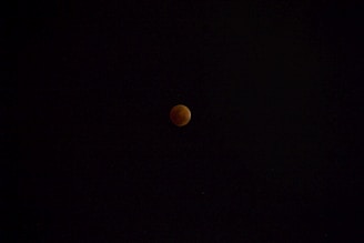 A lunar eclipse with the moon appearing in a dark sky, showing a reddish hue due to the Earth's shadow.