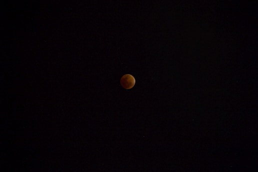A lunar eclipse with the moon appearing in a dark sky, showing a reddish hue due to the Earth's shadow.