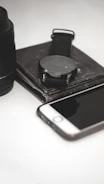 A stylish watch on a dark leather strap resting beside a sleek smartphone and notebook.