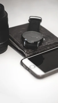 A stylish watch on a dark leather strap resting beside a sleek smartphone and notebook.