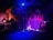 A dimly lit stage with musical instruments, including a drum set, two electric guitars, and a keyboard. The backdrop features the words 'Rock City' in bold letters with a stylized design. The lighting creates a moody ambiance, with blue and purple hues dominating the scene.