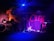 A dimly lit stage with musical instruments, including a drum set, two electric guitars, and a keyboard. The backdrop features the words 'Rock City' in bold letters with a stylized design. The lighting creates a moody ambiance, with blue and purple hues dominating the scene.