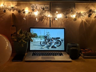 A cozy desk setup illuminated by moonlight, with astrology charts and a glowing laptop screen in dark mode.