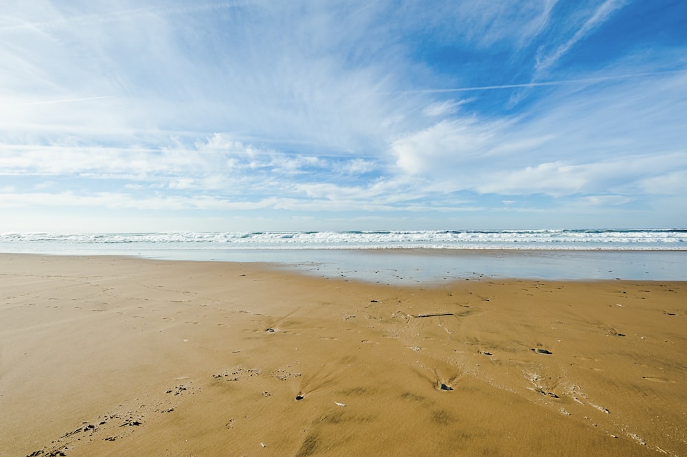 brown sand and body of water under blue sky