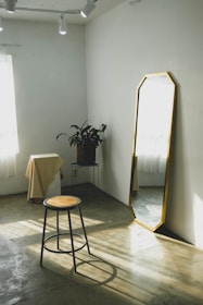 A sleek full-length wall mirror with a minimalist frame reflecting a sunlit bedroom corner.