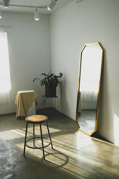 round brown wooden stool near leaning mirror