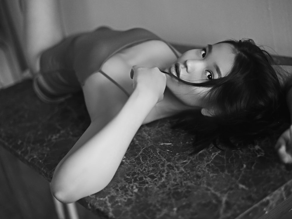 grayscale photography of woman lying on tile sink