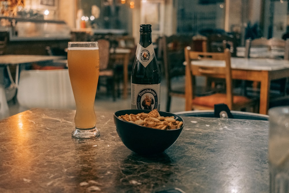 pilsner glass filled with beer beside bowl of chips on marble table