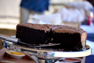 Chocolate cake with silky chocolate frosting, styled with matte gold cutlery on a soft beige surface.