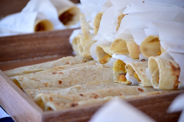 Flatbreads filled with assorted ingredients, partially wrapped in white paper, are neatly arranged in a wooden tray.