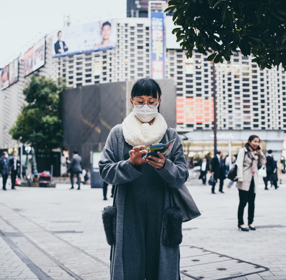 woman in grey dress wearing face mask fiddling on her phone at the park