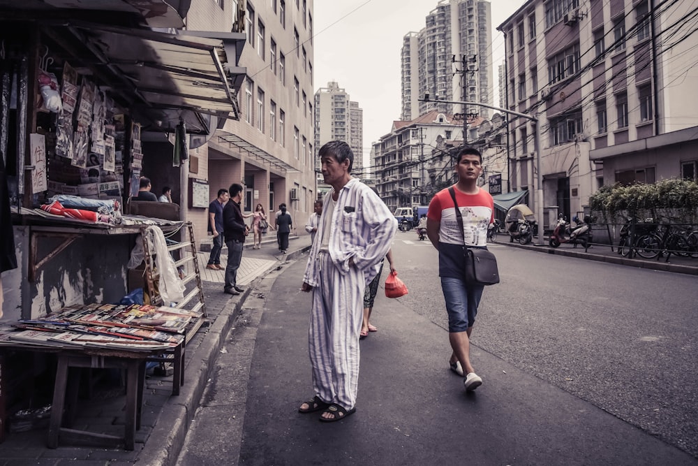 Mann im grau-weißen Pyjama steht vor Zeitschriftenstand an der Straße