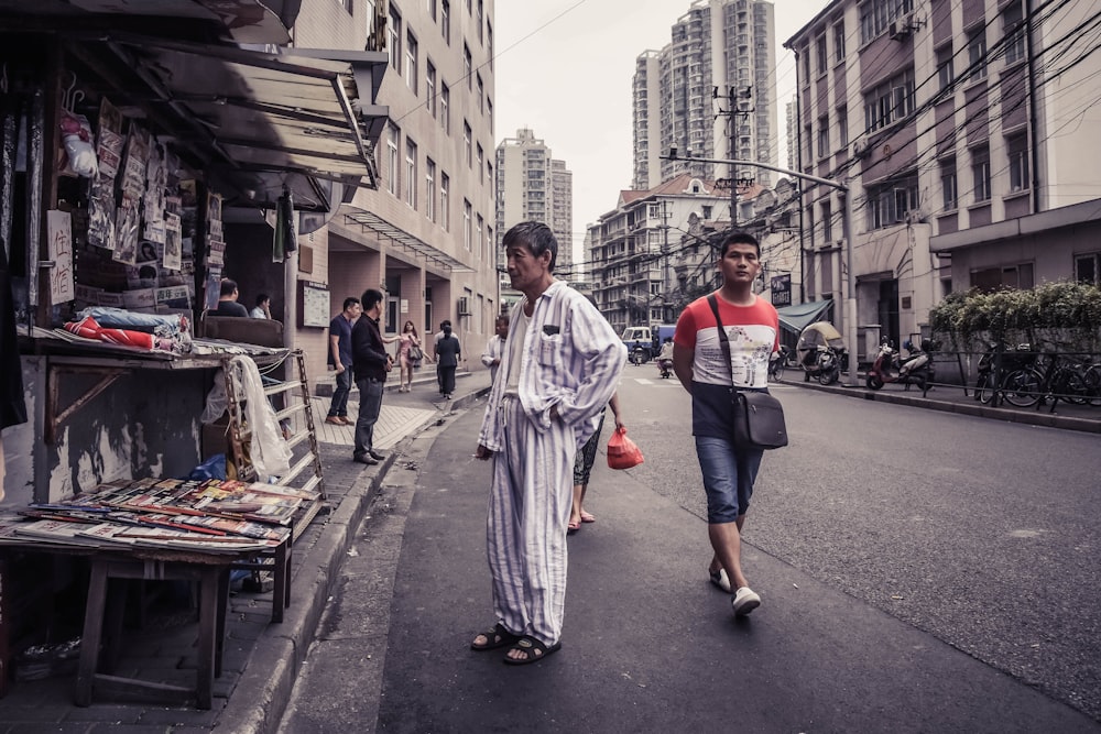 man in grey and white pajama standing in front of magazine stall by the street