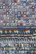 A collection of colorful and varied souvenirs arranged on display. The top section features a series of tiles with intricate patterns and illustrations, many labeled with 'Lisboa' or 'Lisbon Portugal'. Below the tiles, there are magnets shaped like roosters, trams, and traditional bottles with detailed designs. The display exudes a sense of Portuguese culture and heritage.
