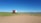 A red truck with a white cargo area is parked on an open plain with sparse grass and dirt. A clear blue sky extends above, with mountains visible in the background near a lake. The landscape is vast and uninhabited, conveying a sense of solitude and wilderness.