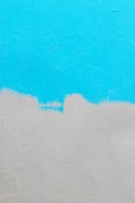 A textured wall painted with two colors. The upper part of the wall is painted in a bright cyan color, while the lower part is painted in a light gray. There is an uneven, wavy border where the two colors meet.