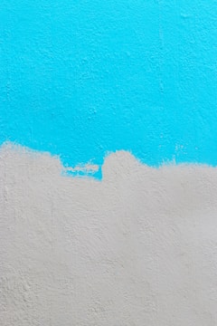 A textured wall painted with two colors. The upper part of the wall is painted in a bright cyan color, while the lower part is painted in a light gray. There is an uneven, wavy border where the two colors meet.