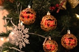 Ornate Christmas tree with personalized red and gold ornaments featuring names, surrounded by green pine branches and decorated with a silver snowflake and string lights.