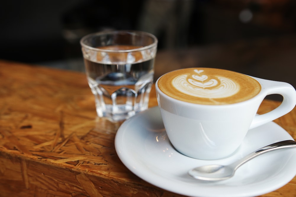 white ceramic teacup near drinking glass on brown surface