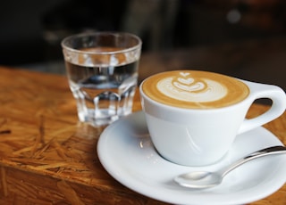 white ceramic teacup near drinking glass on brown surface