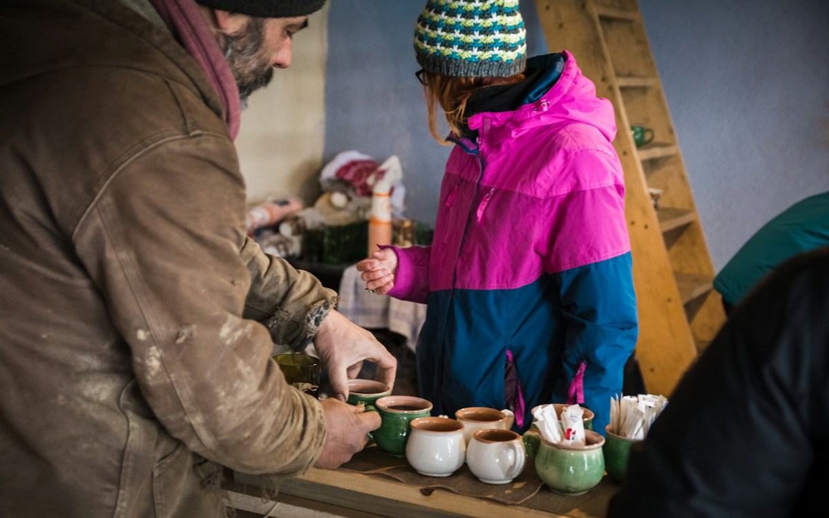 Un vendeur sert du vin chaud dans des tasses en céramique à une cliente emmitouflée, sur un stand de marché de Noël