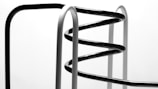 Curved metal bars, possibly part of a modern sculpture or furniture piece, are arranged in a spiral formation with both black and white segments against a neutral background.