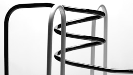 Curved metal bars, possibly part of a modern sculpture or furniture piece, are arranged in a spiral formation with both black and white segments against a neutral background.