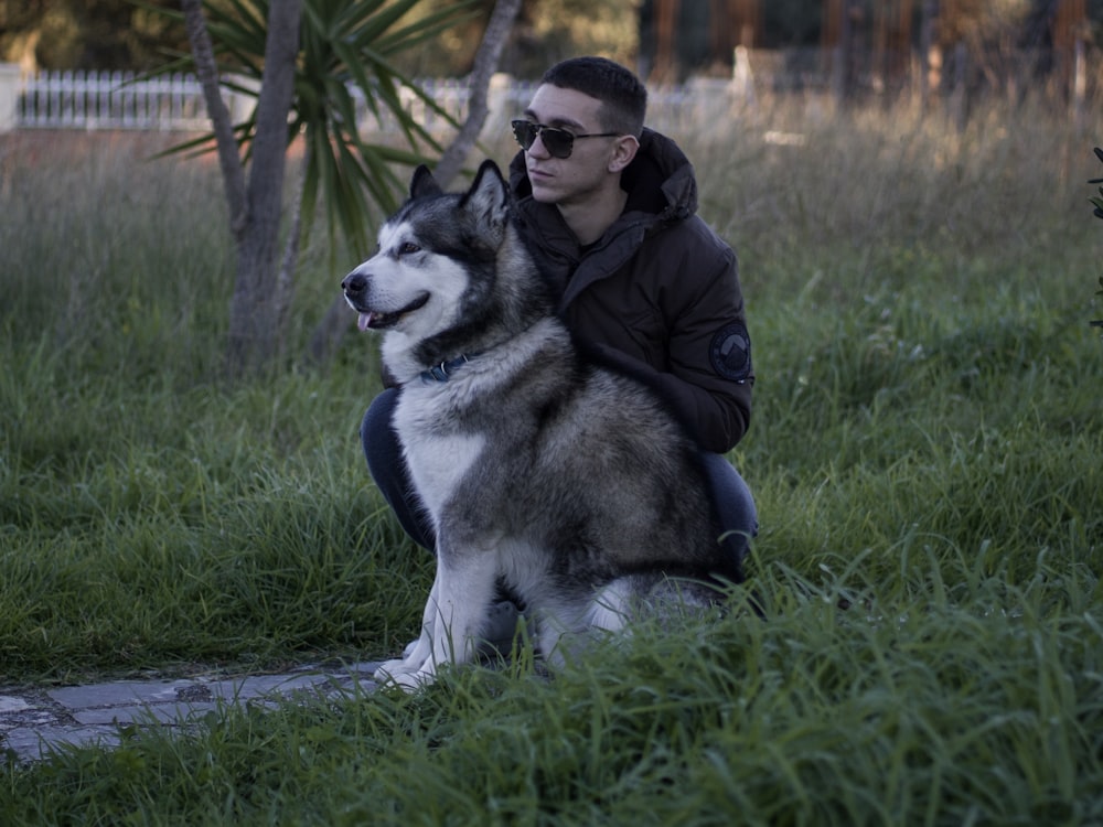 man sitting beside Siberian Husky outdoor during daytime