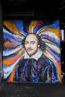 A colorful mural painted on a brick wall, depicting a historical figure with a ruffled collar. The background features a swirl of vibrant colors including blue, yellow, and purple, creating a dynamic and artistic atmosphere.