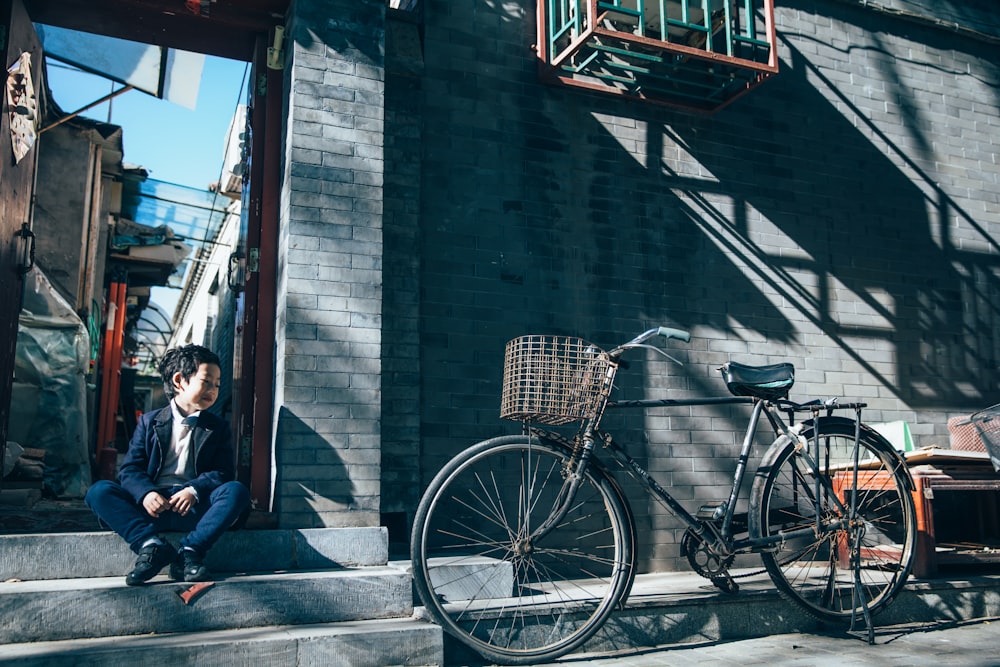 boy sitting near parked bicycle