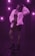 A person poses confidently in a dimly lit environment, accented by a vibrant purple light. They wear a plush white fur coat over a fitted dress and heart-shaped sunglasses, adding to the glamorous and stylish look. The atmosphere suggests a lively, club-like setting.