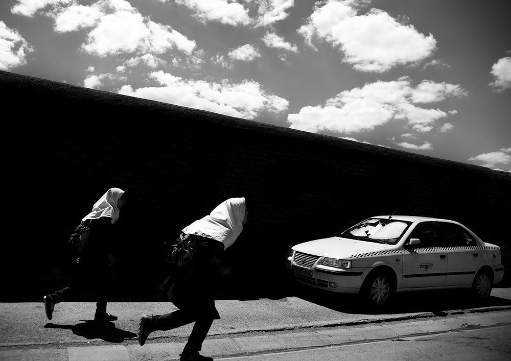 two persons running on street near car