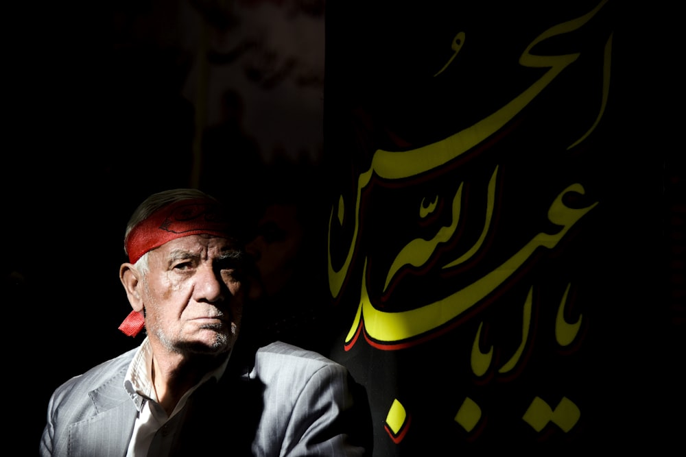 man in black jacket beside a flag with Arabic script text