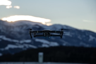 A fixed-wing UAV soaring high above mountainous terrain with the sun setting behind.