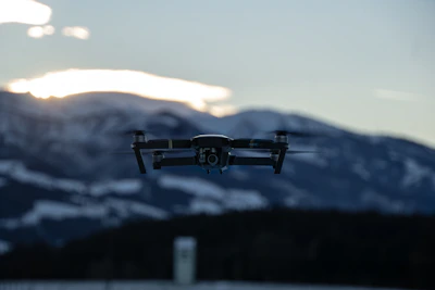 A drone hovering over a forested mountain landscape during golden hour.
