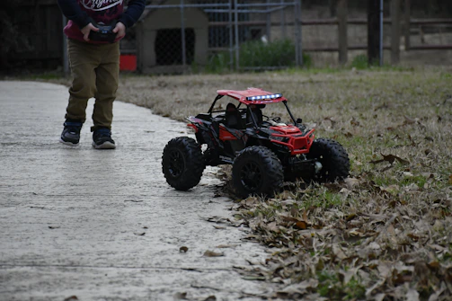 A child playing with a remote-controlled car on a sunny backyard driveway.