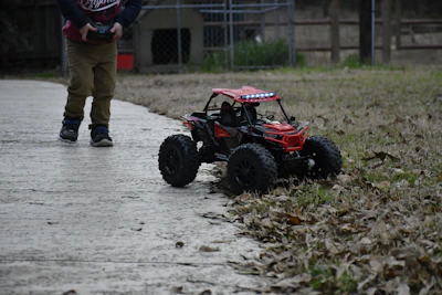 A smiling child holding a remote control car racing across a sunny garden path.