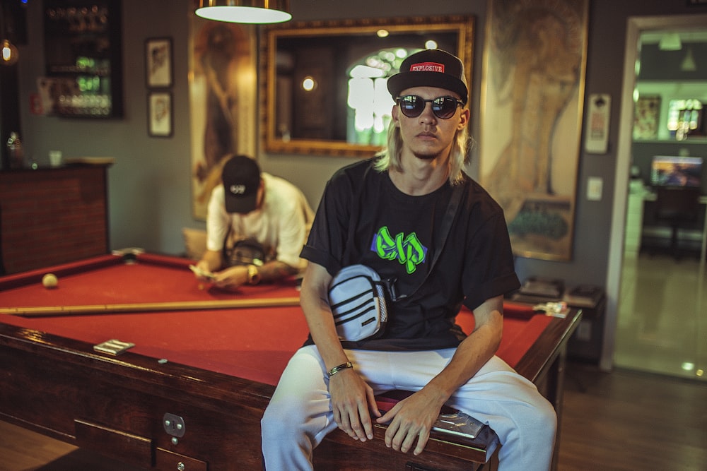 man sitting on billiard table with man nearby