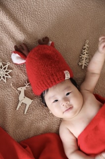 A baby bundled in a cozy holiday-themed onesie with tiny candy cane prints, lying on a soft blanket.