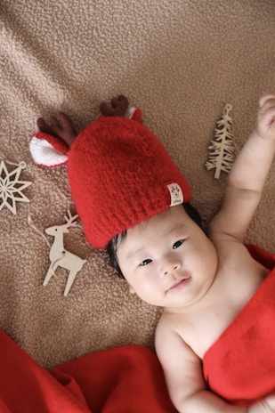 A baby bundled in a cozy holiday-themed onesie with tiny candy cane prints, lying on a soft blanket.