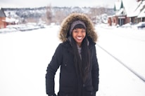 A smiling person wrapped in a chunky knit scarf, standing in a snowy park.