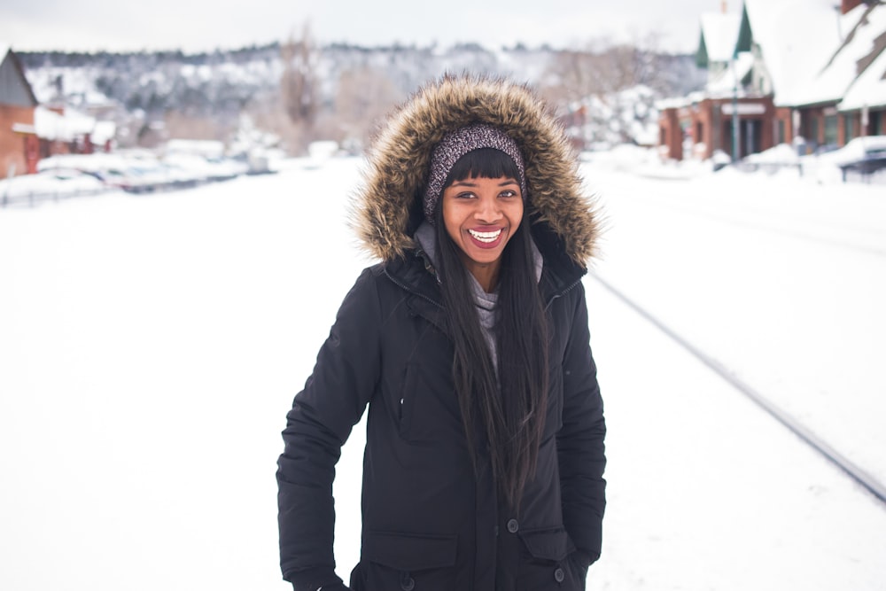 donna che indossa cappotto in piedi sulla neve e sorridente durante il giorno