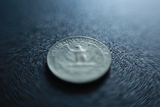 A sleek coin gimmick displayed with soft shadows on a deep charcoal background.