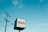 A cube-shaped sign with the word 'SURGERY' in red letters on a white background. Nearby, a tall utility pole and several power lines stretch across a bright blue sky with scattered clouds.