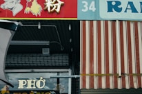 A storefront with a red and white striped awning and signage featuring images of a cow and a chicken. The word 'PHO' is prominently displayed on a window below the awning. The numbers '34' and the text 'RAN' are visible above.