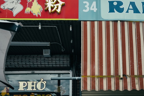 A storefront with a red and white striped awning and signage featuring images of a cow and a chicken. The word 'PHO' is prominently displayed on a window below the awning. The numbers '34' and the text 'RAN' are visible above.