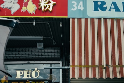A storefront with a red and white striped awning and signage featuring images of a cow and a chicken. The word 'PHO' is prominently displayed on a window below the awning. The numbers '34' and the text 'RAN' are visible above.
